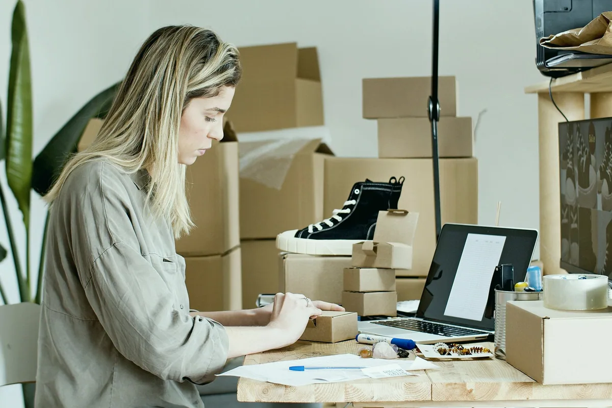 Laptopta e-ticaret satıcı panelini inceleyen kişi ve yanında kargo paketleri