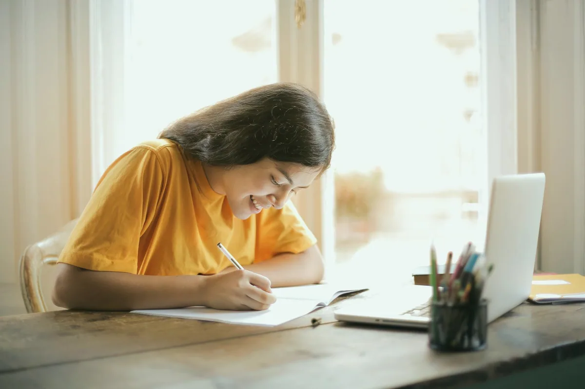 Defter ve dizüstü bilgisayarla ders çalışan öğrenci